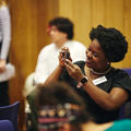 A woman sitting in the audience at a conference taking a photo